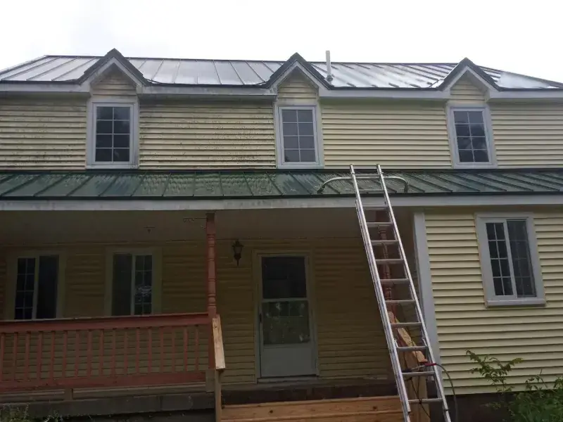 A large farmhouse with algae-streaked siding and roof before cleaning